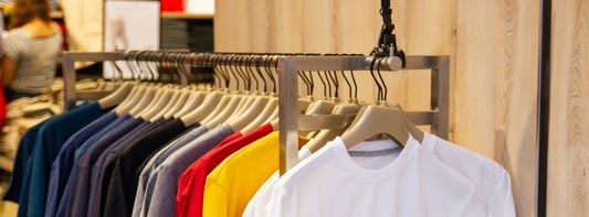 Une série de tee-shirts pendus avec des cintres sur une barre danss un magazin